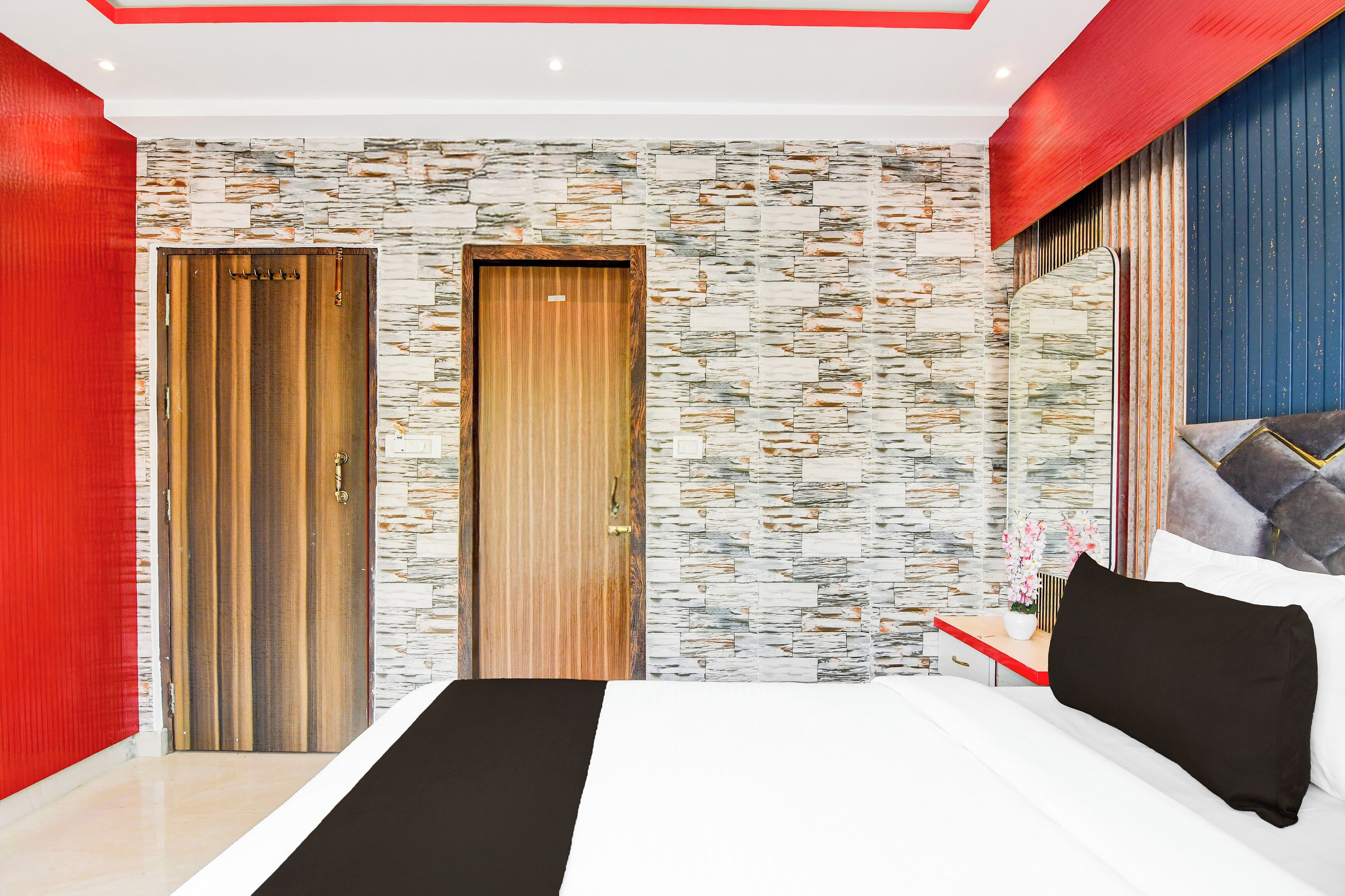Un dormitorio moderno con una cama grande, dos puertas, una pared con textura de piedra y una pared de acento roja.