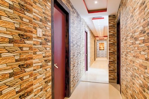 A corridor with stone-patterned walls and doors, leading to a room with a Buddha statue. - OYO 834317 Love Point (Kolkata)