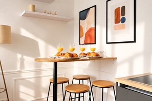 A modern kitchen with a dining table set for breakfast, featuring croissants and orange juice glasses. - Charming Flat near Opéra Garnier (Paris)