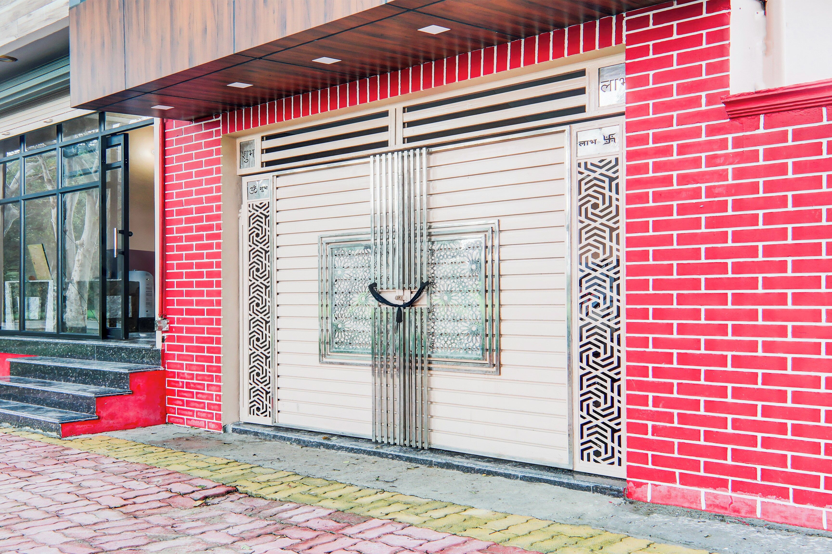A red brick building with a large metal gate, a window with a geometric pattern, and a door with a similar design.