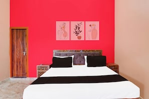 A bedroom with a red wall, a wooden door, a bed with black and white bedding, and three framed pictures above the bed. - Hotel O Kashvi Hotel (Misrikh)