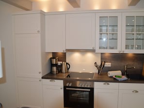 Une cuisine moderne avec des meubles blancs, une cuisinière en acier inoxydable, une machine à café et un meuble vitré placé au-dessus de l’évier.