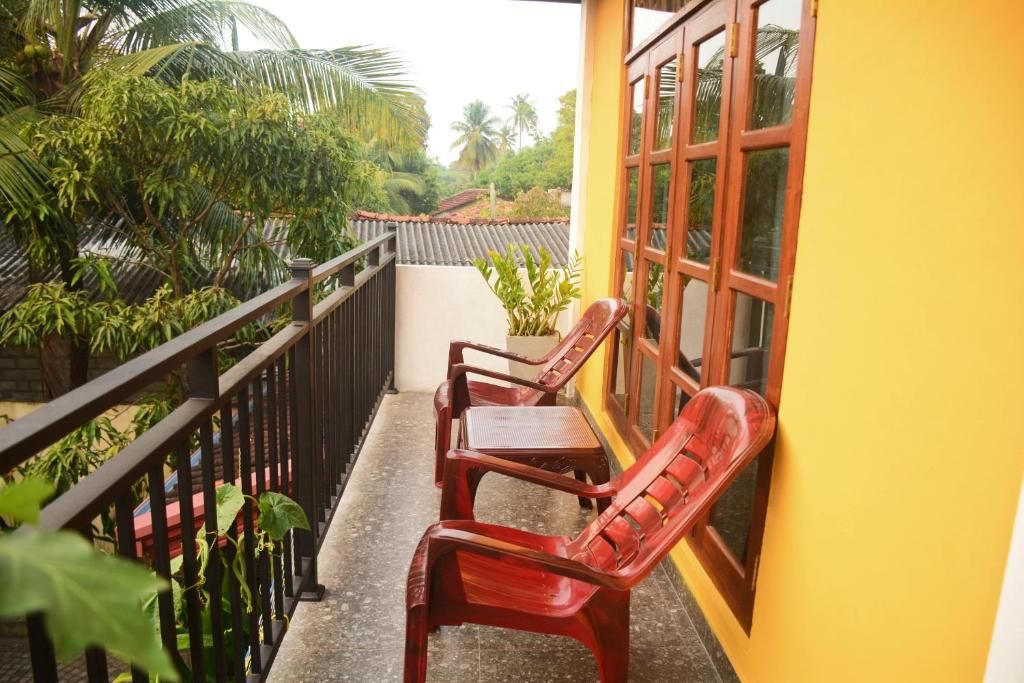 A balcony with two wooden chairs, a railing, and a yellow wall with a window.