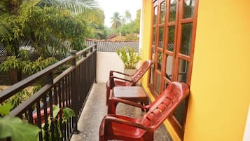 A balcony with two wooden chairs, a railing, and a yellow wall with a window.