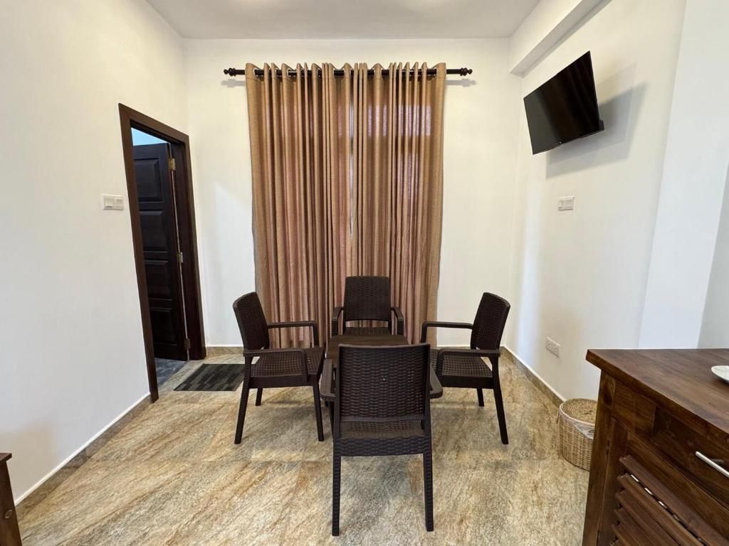 A room with a dining table and chairs, a television mounted on the wall, and a door leading to another room.