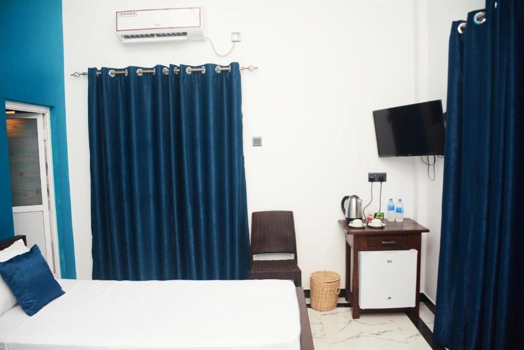Una habitación de hotel con cama, un escritorio pequeño con hervidor, televisor y refrigerador pequeño.