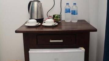 Una kitchenette pequeña con cafetera, dos tazas, un plato, dos botellas de agua y un refrigerador.