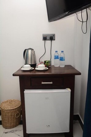 Une petite kitchenette équipée d’une machine à café, de deux tasses, d’une assiette, de deux bouteilles d’eau et d’un réfrigérateur.