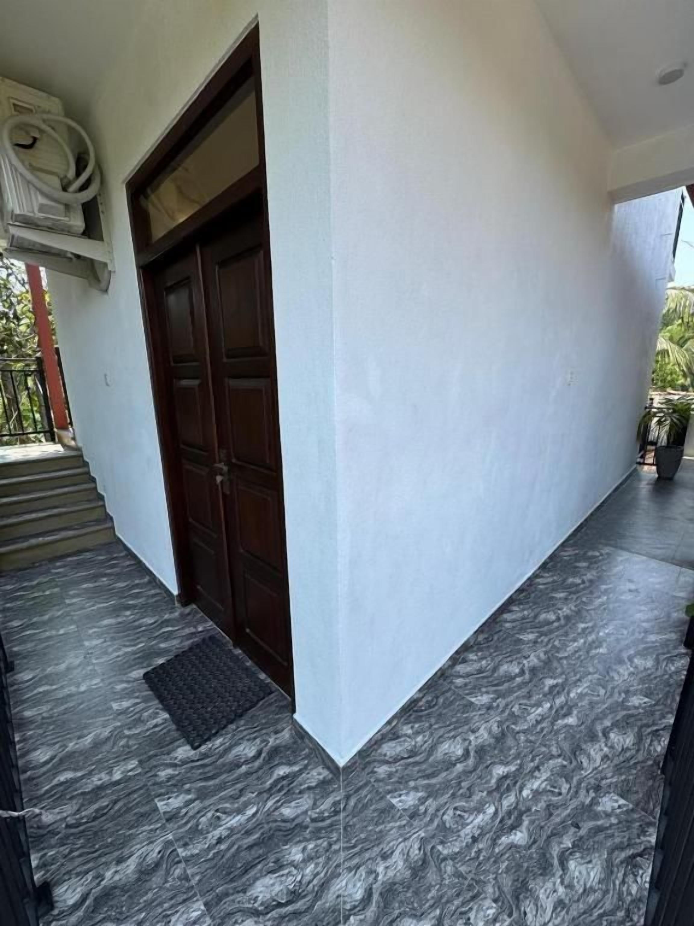 Entrada de un edificio con una puerta de madera oscura, una pared blanca y un piso de mármol gris.