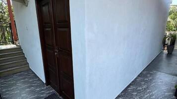 Entrada de un edificio con una puerta de madera oscura, una pared blanca y un piso de mármol gris.