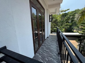 A balcony with a view of a garden and a building with large windows. - Ayubowan Homestay Katunayake (Katunayake)