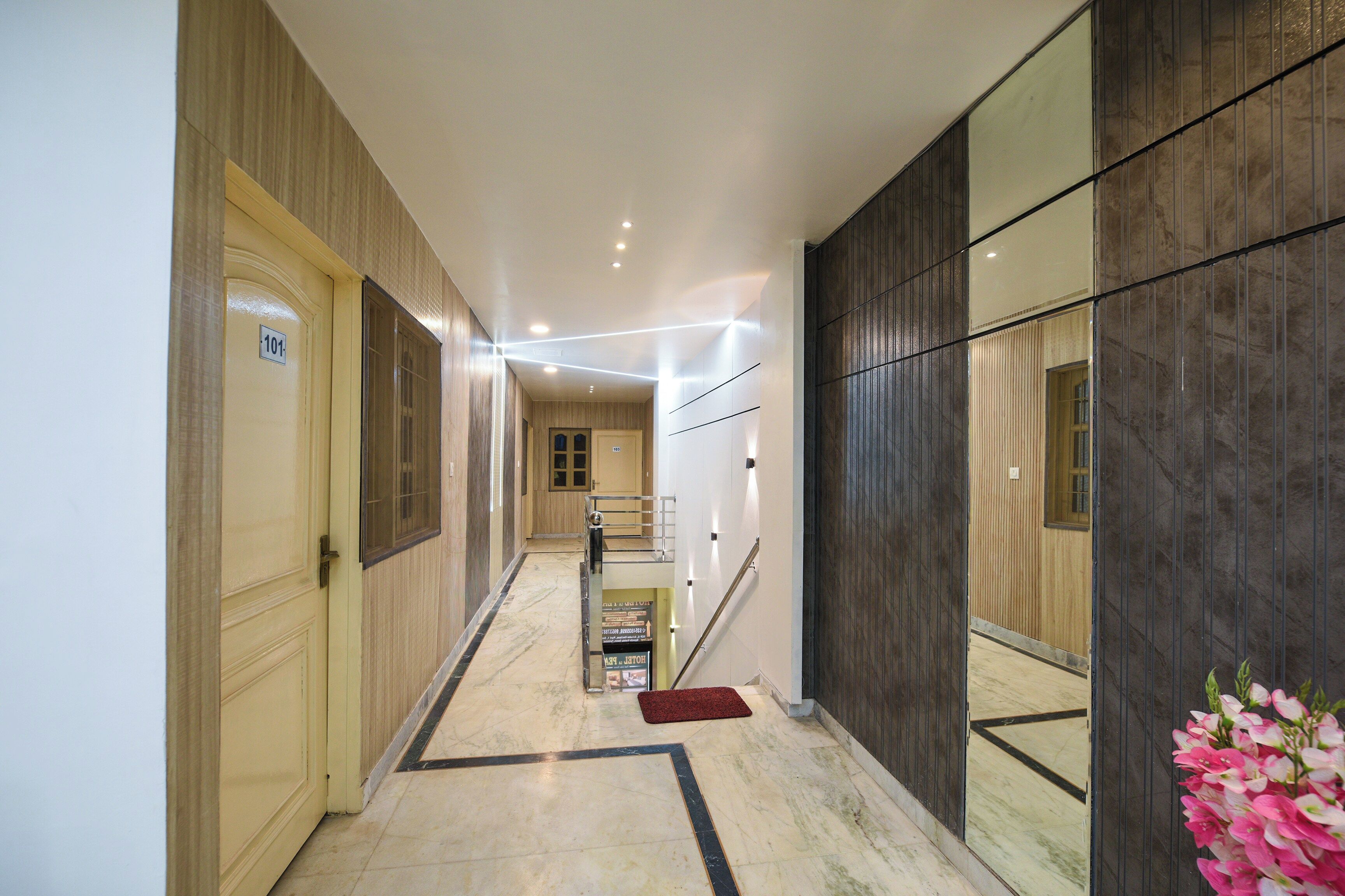 A hallway with a wooden door labeled '101', a staircase, and a red mat at the bottom.