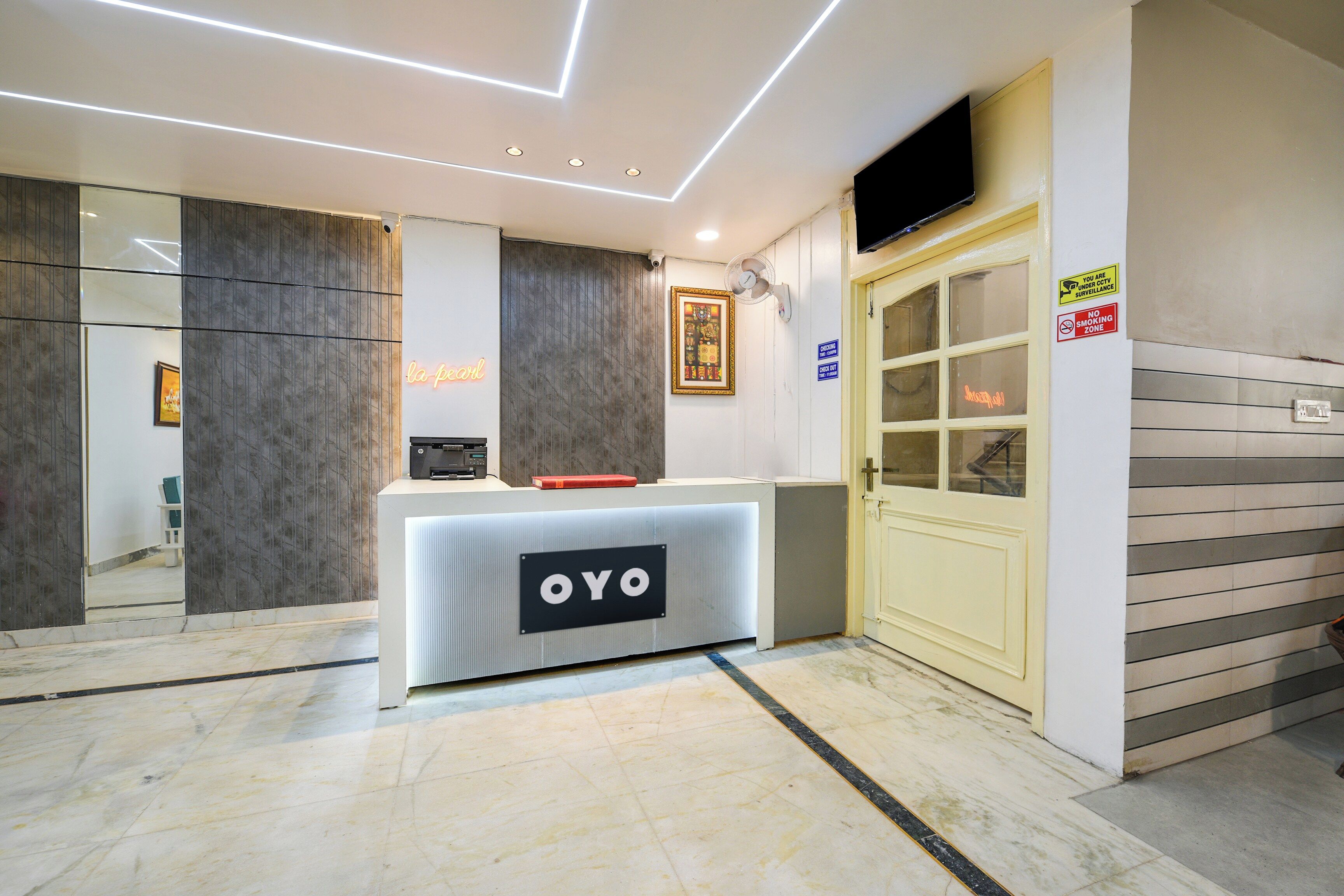 Un espace d’accueil au design moderne, comprenant un comptoir de réception portant l’inscription « OYO », un guichet d’enregistrement, une caméra de surveillance et un panneau indiquant la présence d’un système de vidéosurveillance.