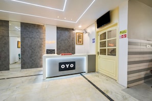 A reception area with a modern design, including a reception desk labeled 'OYO,' a check-in counter, a security camera, and a surveillance sign. - Hotel O Galaxy (Faridabad)