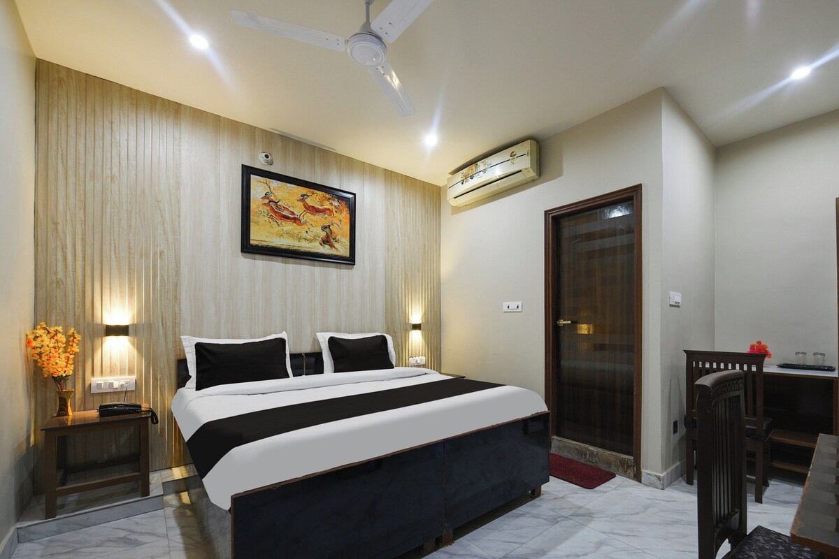 Quarto de hotel com cama, quadro, ar condicionado, escrivaninha e cadeira.