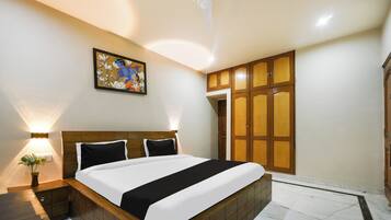 Habitación de hotel con cama, mesita de noche, lámpara de pared, ventilador de techo y puerta con panel de madera.