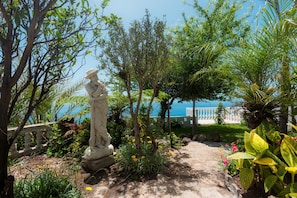 A garden with a statue, various plants, and a view of the sea. - BLUE OCEAN VILLA with Private Heated Pool. Magnificent Seaview. AC, WIFI, Garden (Fajã da Ovelha, Calheta)