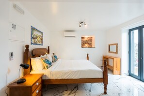 Ein Schlafzimmer mit einem Bett, Nachttisch, Lampe, Wandbild, Klimaanlage und Blick durch ein Fenster.