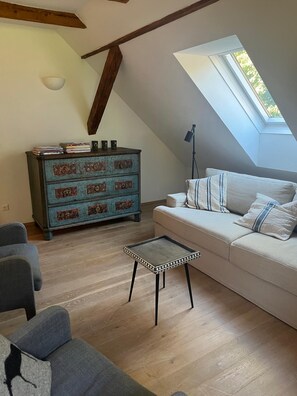 A loft-style living room with a sloped ceiling, a wooden beam, a sofa with striped pillows, a small coffee table, and a vintage chest of drawers. - New Listing (Bodensdorf)