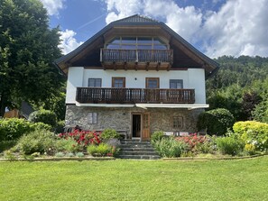 A two-story chalet with a stone facade, wooden balcony, and a well-maintained garden. - New Listing (Bodensdorf)