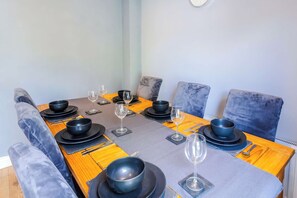 A dining table set with black bowls, wine glasses, and cutlery, surrounded by grey upholstered chairs. - stylish 3BD house - free parking - smart tv (Bristol)