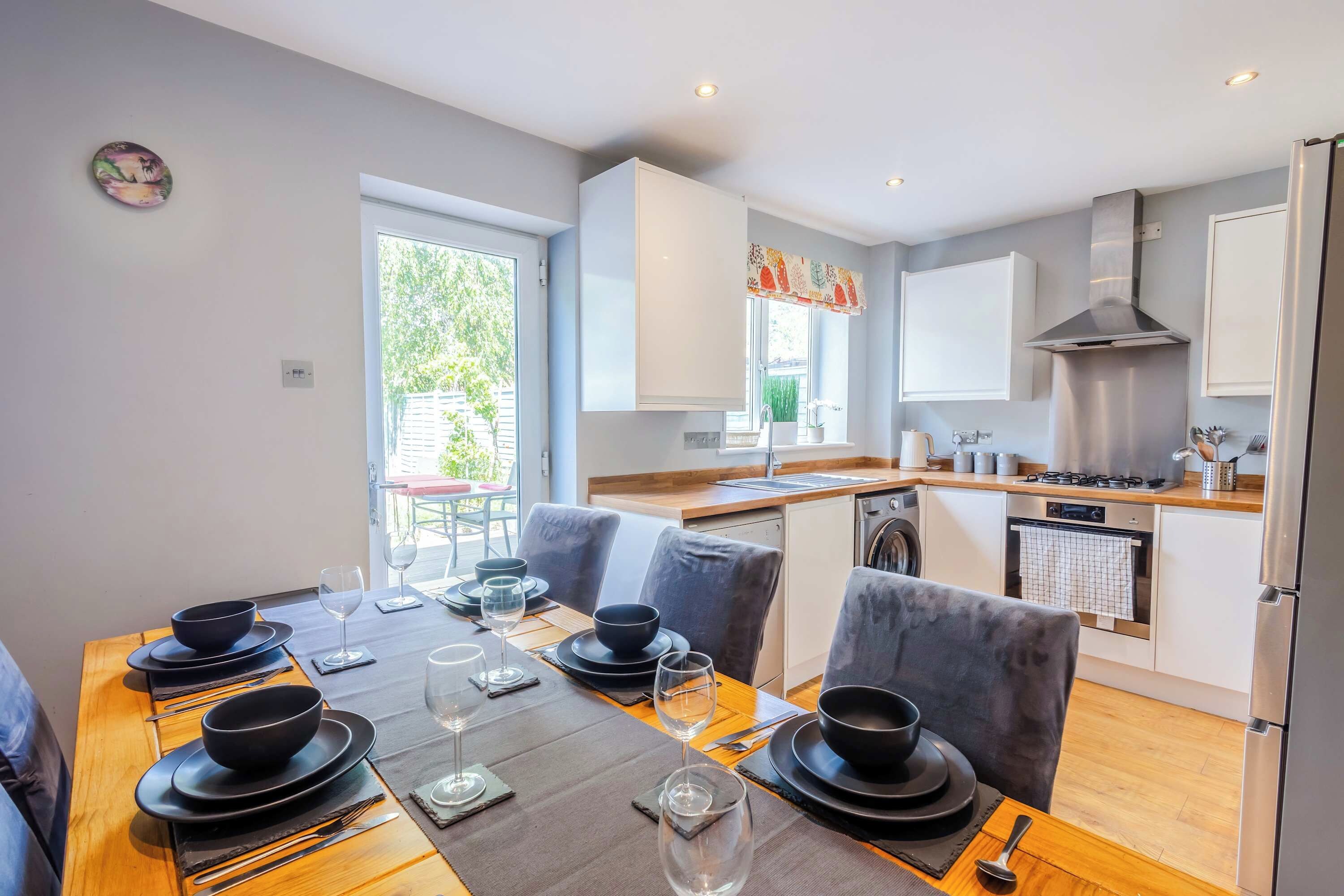 A modern kitchen with white cabinets, a stainless steel range hood, and a dining area with a wooden table set for four.