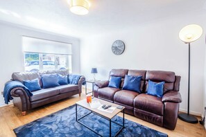 A living room with two leather sofas, a coffee table, a floor lamp, a wall clock, and a large window. - stylish 3BD house - free parking - smart tv (Bristol)