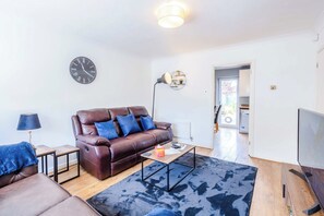 A modern living room with a leather sofa, a coffee table, a clock, and a television. - stylish 3BD house - free parking - smart tv (Bristol)