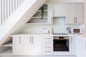 A compact kitchen with white cabinetry, a built-in oven, a microwave, and a toaster. - Cosy 3 Bed | Sleeps 7 | Free Parking (Bristol City)