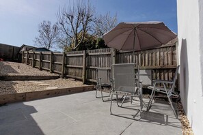 A patio area with a wooden fence, a concrete floor, and a metal umbrella. - Cosy 3 Bed | Sleeps 7 | Free Parking (Bristol City)