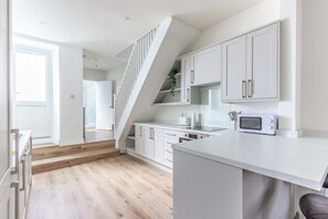 A modern kitchen with white cabinetry, a wooden staircase, and a built-in microwave. - Cosy 3 Bed | Sleeps 7 | Free Parking (Bristol City)