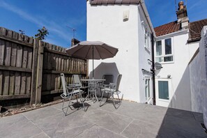 A patio with a table and chairs, a wooden fence, and a white building with a tiled roof. - Cosy 3 Bed | Sleeps 7 | Free Parking (Bristol City)