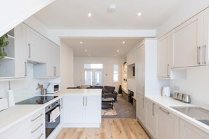 A modern kitchen with white cabinetry, a central island, and a dining area with a sofa and a coffee machine. - Cosy 3 Bed | Sleeps 7 | Free Parking (Bristol City)