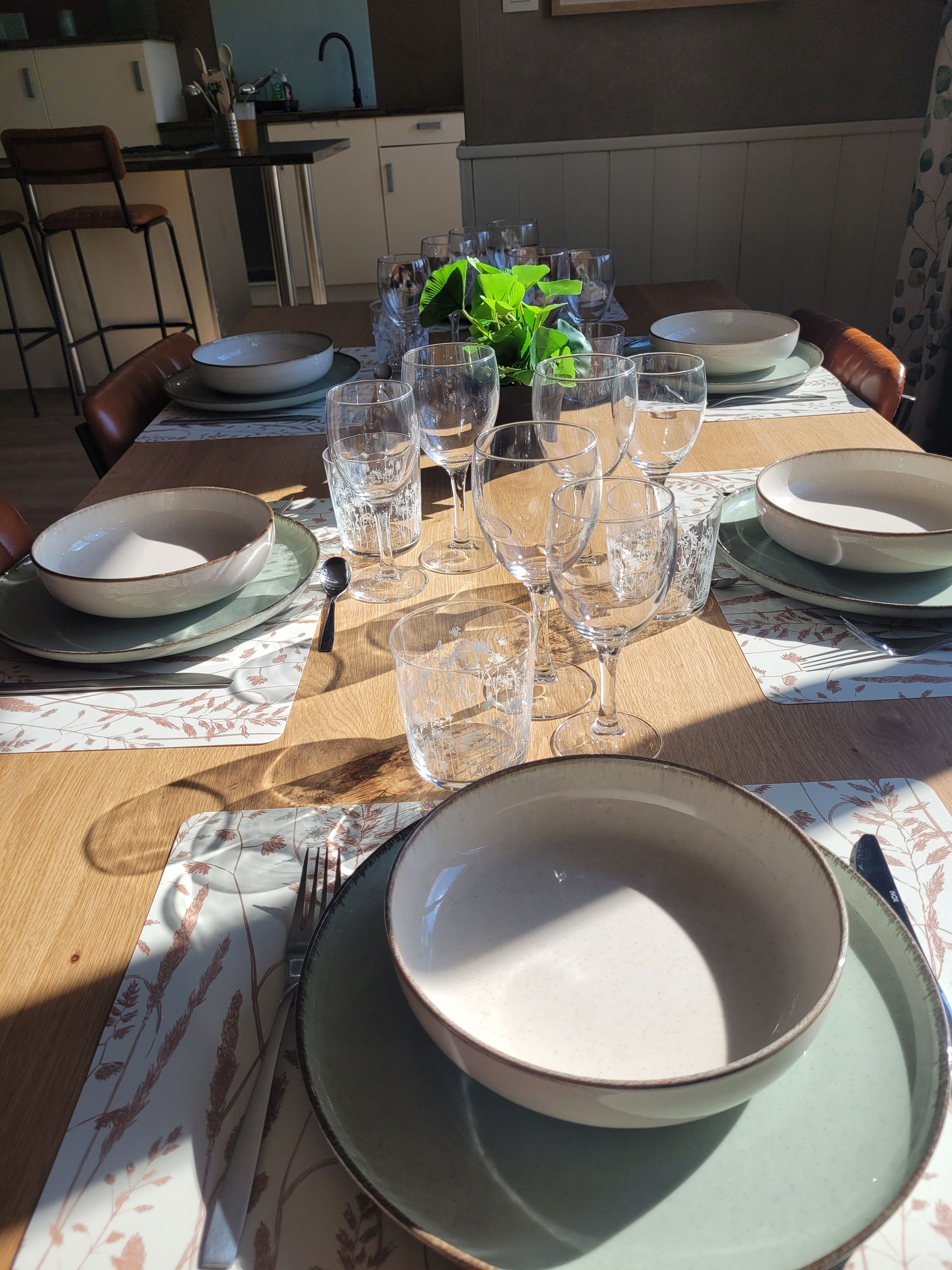 Une table à manger dressée avec des assiettes, des verres et des couverts, entourée de chaises.