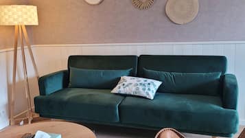 Un salon avec un canapé vert, une table basse ronde, un fauteuil en cuir marron et des œuvres d’art décoratives accrochées au mur.