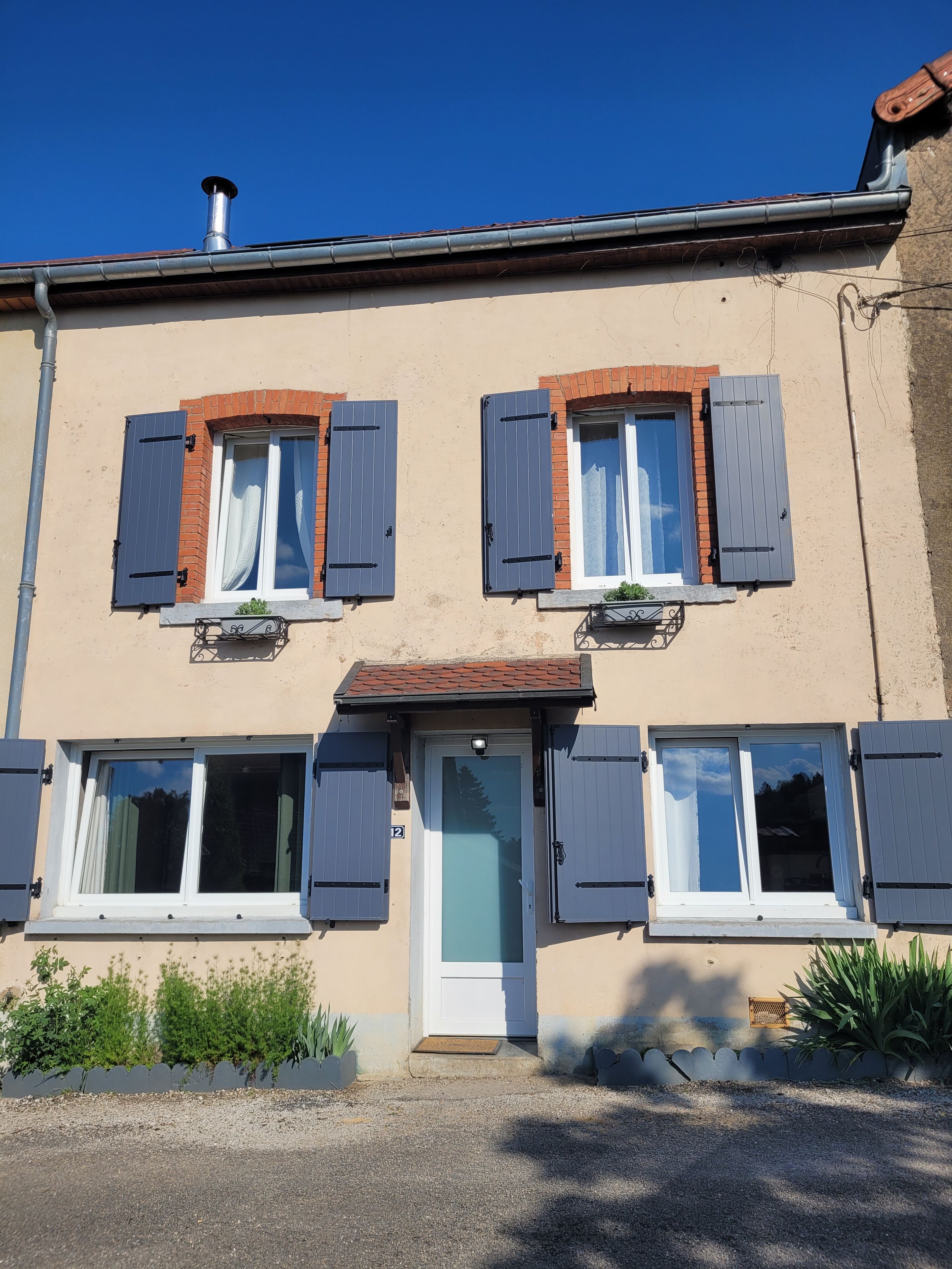 Un bâtiment à deux étages avec une façade beige, de nombreuses fenêtres dotées de volets et une porte bien visible.