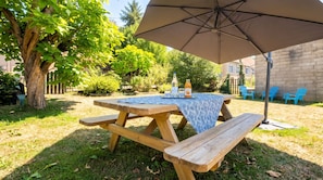 Una mesa de picnic de madera con mantel, una sombrilla y una botella de bebida encima.
