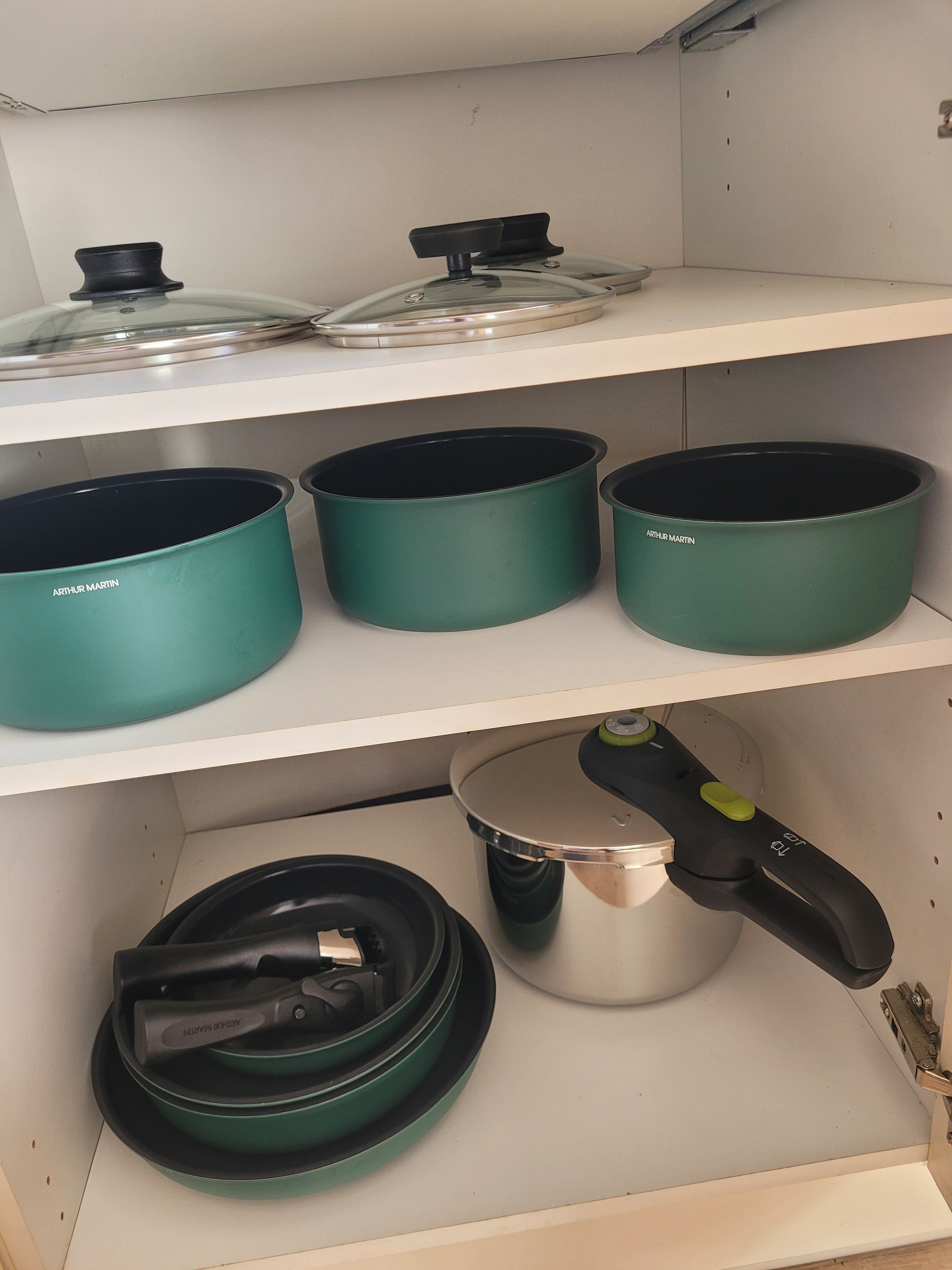 Une cuisine avec trois étagères, chacune contenant des casseroles et des poêles.