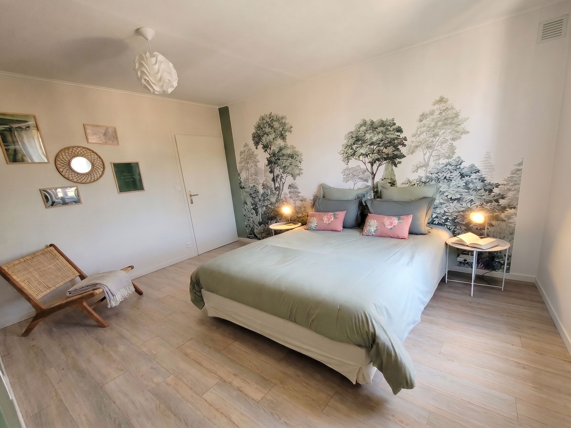 A bedroom with a bed, a chair, a small table, and wall decorations including a mirror and framed pictures.