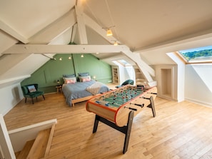 Un dormitorio tipo loft con piso de madera, una cama con almohadas, una pared verde, una mesa de futbolín y un tragaluz.