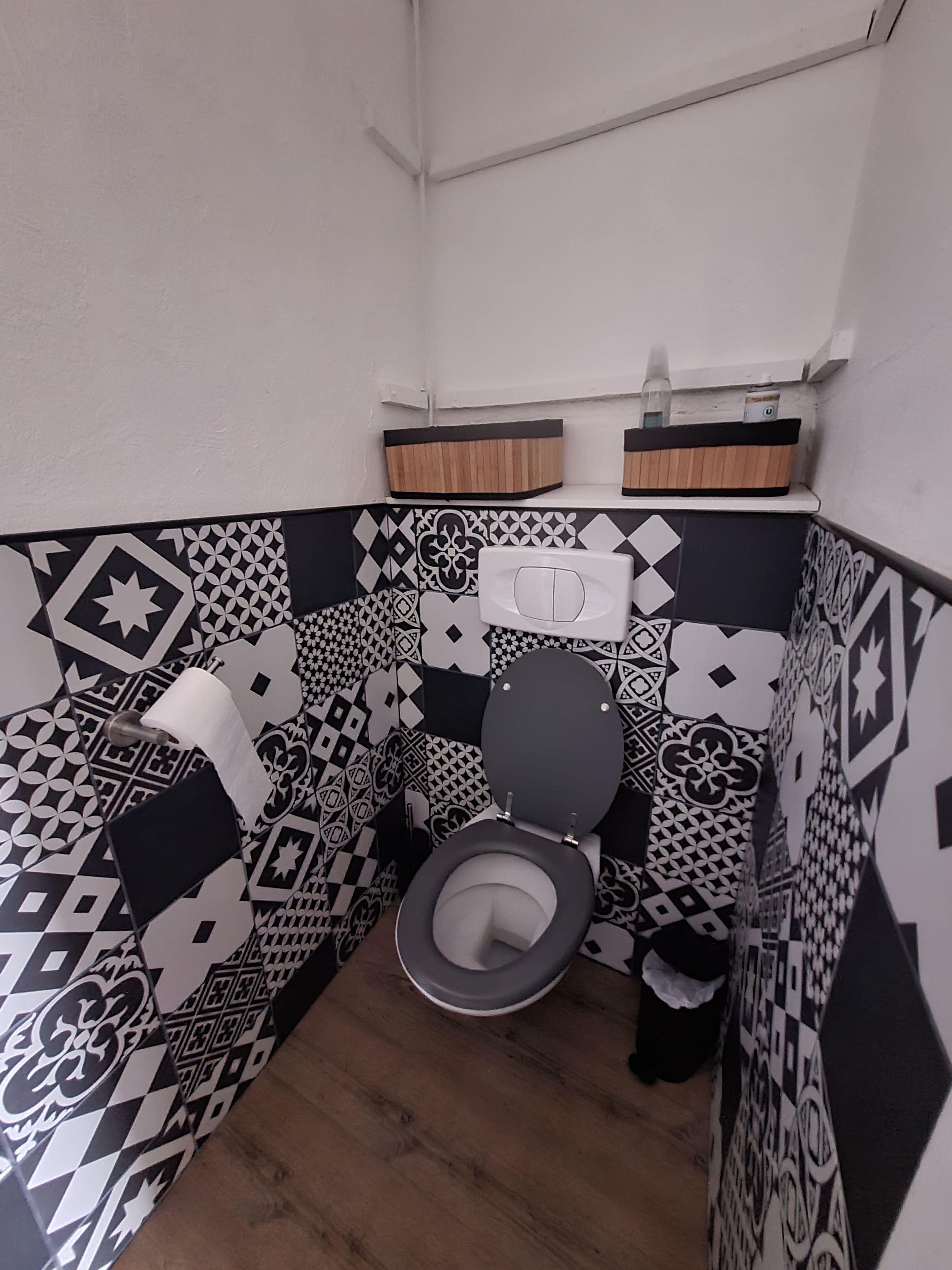 Un bagno con il water, piastrelle decorate e pavimento in legno.