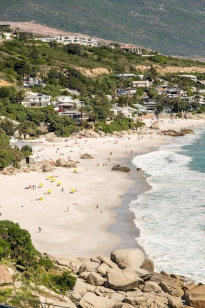 Ein Küstenstrand mit felsigem Gelände, einem Sandstrand und Gebäuden im Hintergrund.