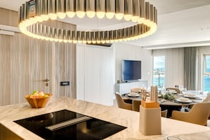 A modern hotel room with a kitchen area, dining setup, and a large TV. - Clifton 2 Bed Apartment Ocean Views Dunmore Noir (Cape Town)