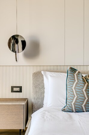A hotel room with a bed, a nightstand, a wall-mounted mirror, and a textured wall panel. - Clifton 2 Bed Apartment Ocean Views Dunmore Noir (Cape Town)