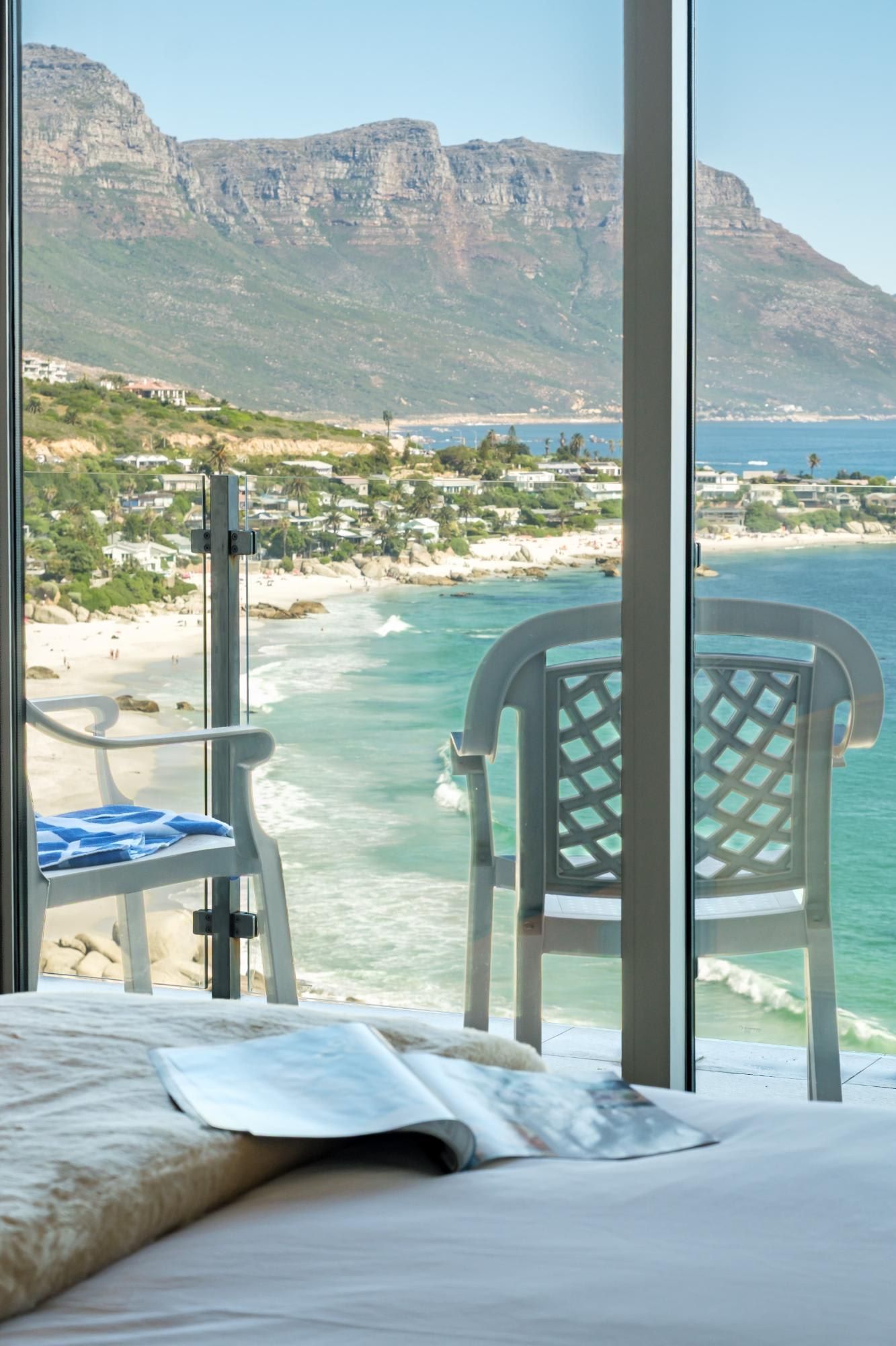 A bed with a view of a beach and mountains through a window.