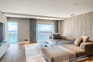 A modern living room with a large window, a sofa set, a coffee table, and a flat-screen TV. - Clifton 2 Bed Apartment Ocean Views Dunmore Noir (Cape Town)