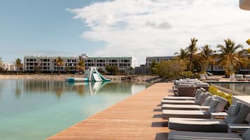 A resort pool area with lounge chairs, a wooden deck, and a building in the background.