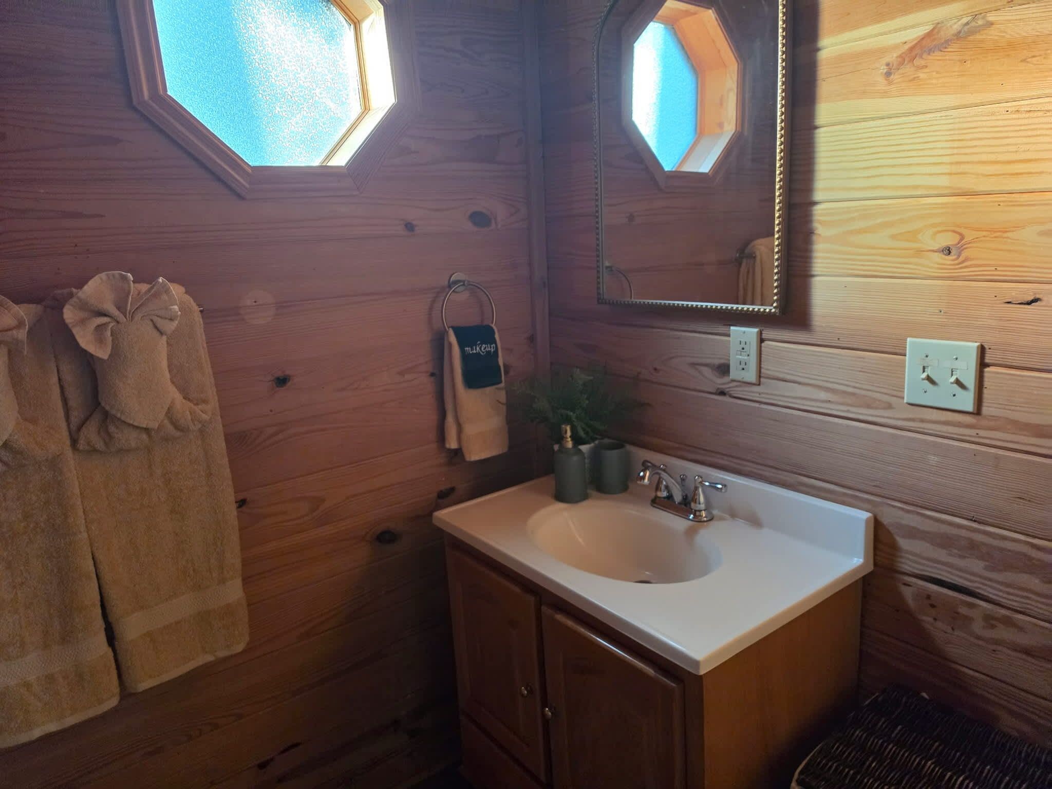 A wooden cabin bathroom with a sink, mirror, towel rack, and a window.