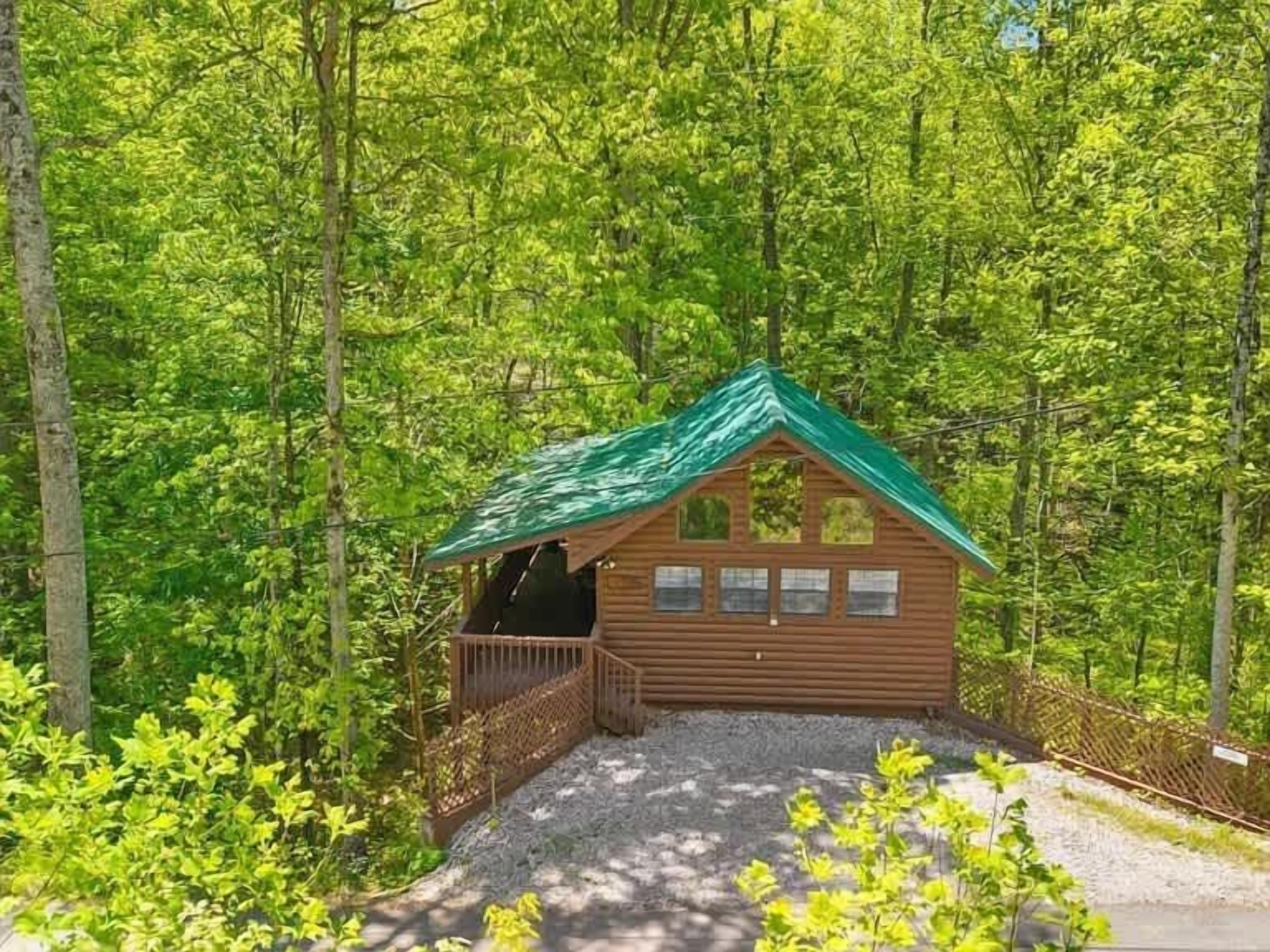 Una cabana de fusta amb teulada verda, envoltada per un bosc dens.