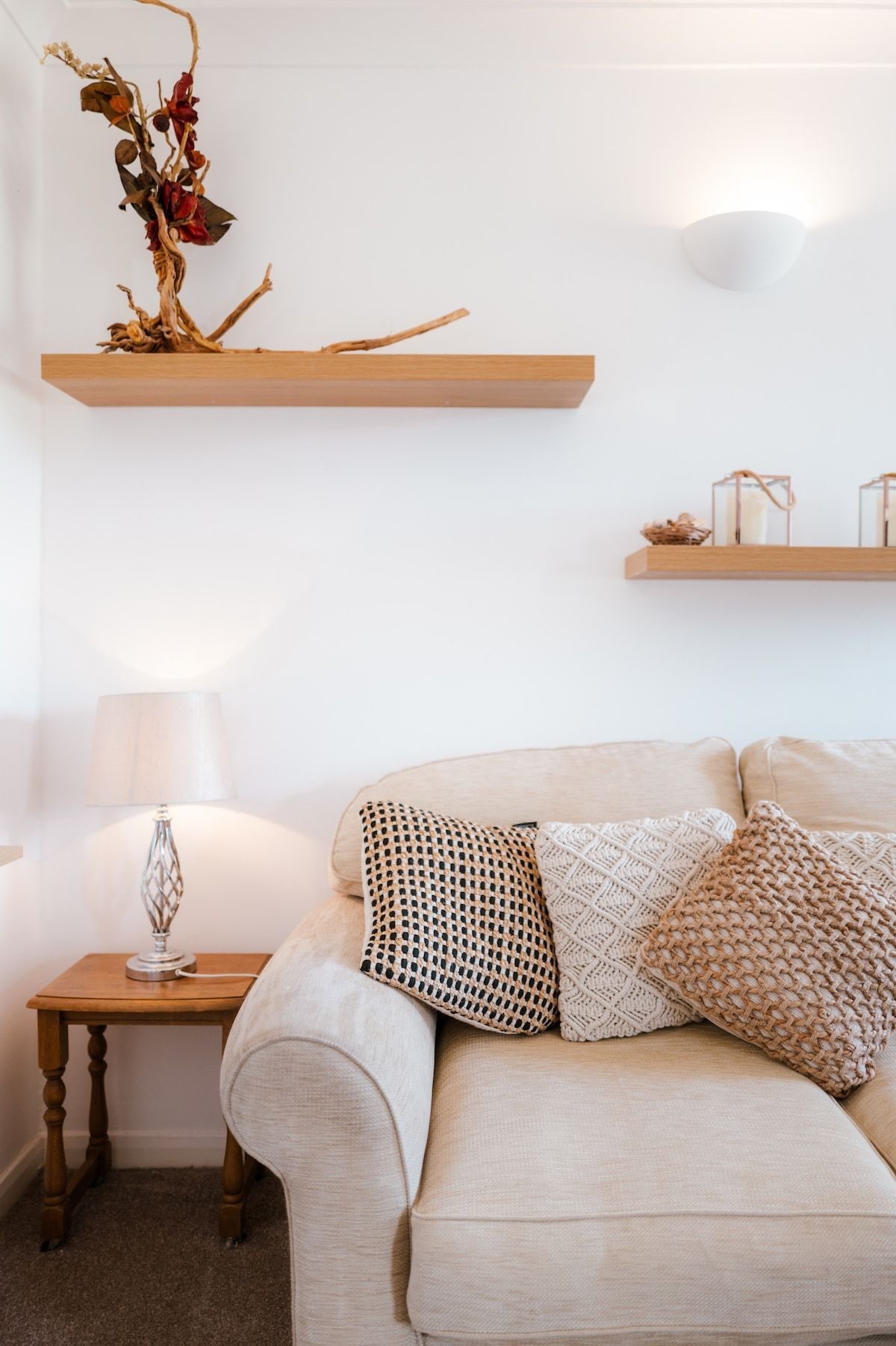 Sala de estar com sofá, luminária, mesinha e duas prateleiras de madeira decoradas.